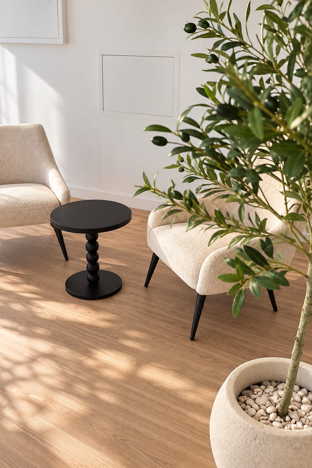 Área de espera com poltronas em tons claros, mesa lateral preta e planta em vaso